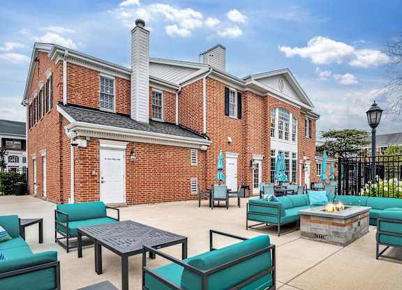 A brick building with a white door and windows, and a patio with green couches and a fire pit.