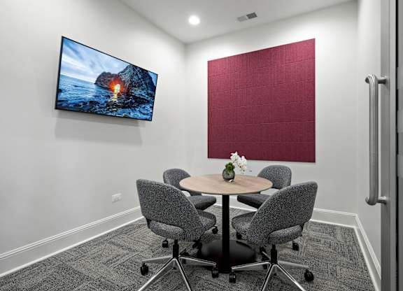 A conference room with a large screen and a table with chairs.