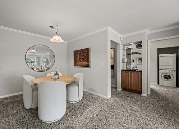 A modern living room with a round table and chairs, a mirror, and a view of the kitchen in the background.