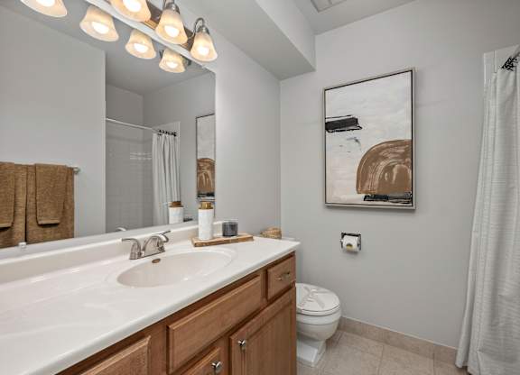 A bathroom with a white sink, toilet, and a painting on the wall.