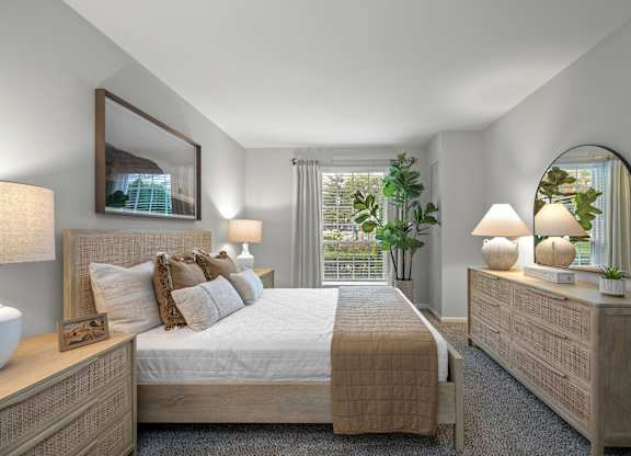 A well-lit bedroom with a large bed, a nightstand with a lamp, and a mirror on the wall.