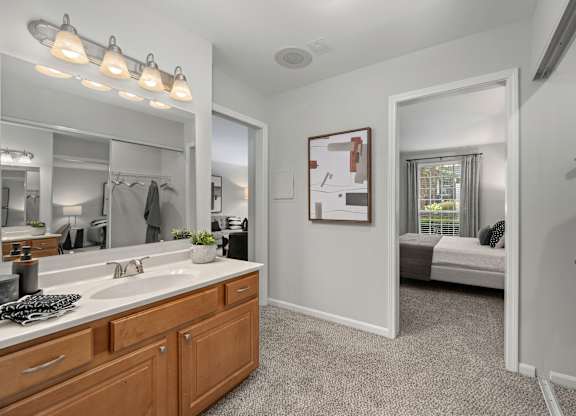 A bathroom with a vanity, mirror, and a bed in the background.