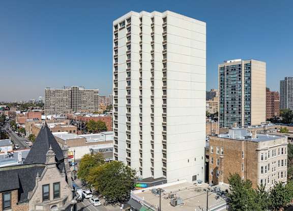 A tall white building with a lot of windows stands in the middle of a city.