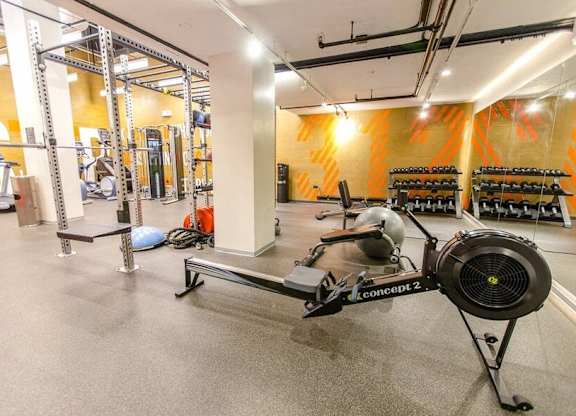 A gym with a rowing machine in the foreground and a wall of shelves in the background.