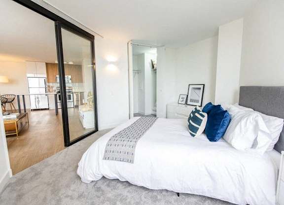 A bedroom with a large bed and a mirrored door leading to a living area.