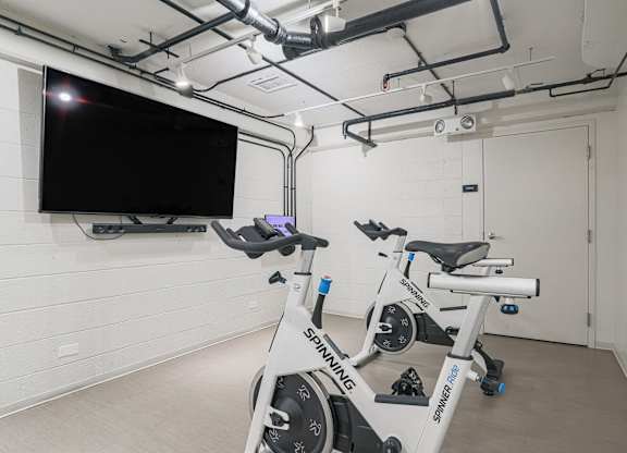 A room with a stationary bike and a television mounted on the wall.