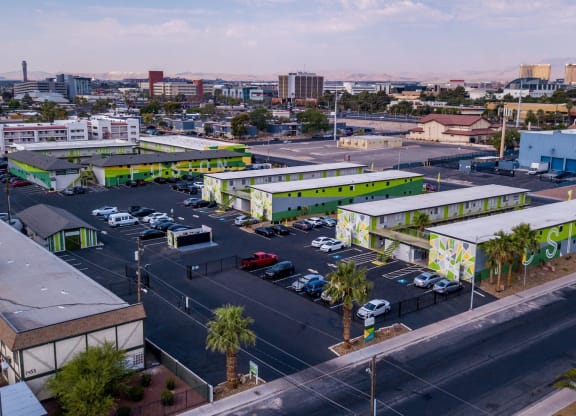 Aerial view of three two-story Fusion Las Vegas apartments in large parking lot filled with cars and Las Vegas skyline in background