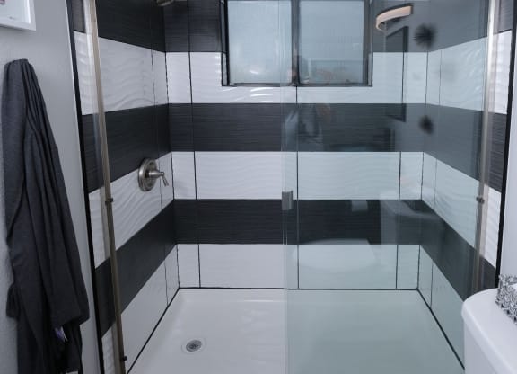 Fusion Las Vegas apartment shower with modern black and white tiles, black grout, sliding glass doors, and chrome plated fixtures.