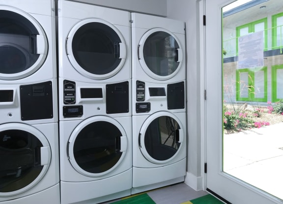 Fusion Las Vegas apartments on site laundry room with six front load washer dryer units next to glass door to courtyard.