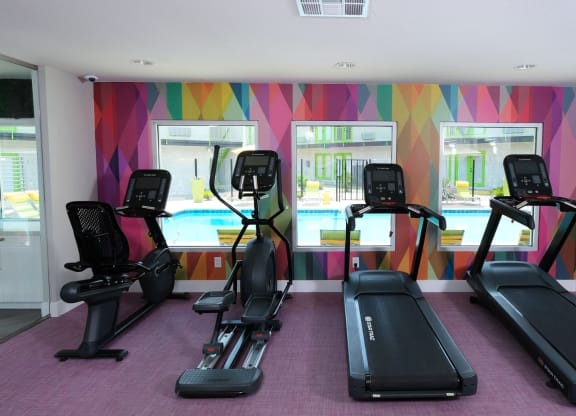 Cardio machines looking out three large windows in a colorful wall in the fitness center at Fusion Las Vegas Apartments, 89119.