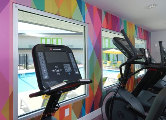 Fusion Las Vegas fitness center with colorful geometric wall and ellipticals looking out large windows toward community pool.