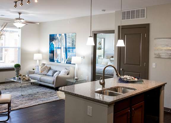 The living room in this updated modern interior at Austin Park Apartments in Miamisburg, Ohio showcases hardwood flooring, granite-style countertops, and a kitchen island, welcoming pets.