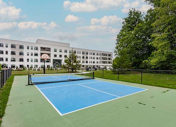 A blue tennis court in front of a white building.