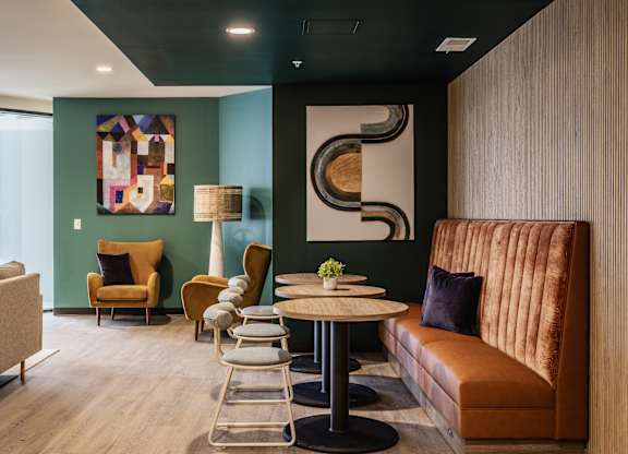 A modern living room is styled with a brown sofa, a circular table, and a prominent abstract painting hanging on the wall.