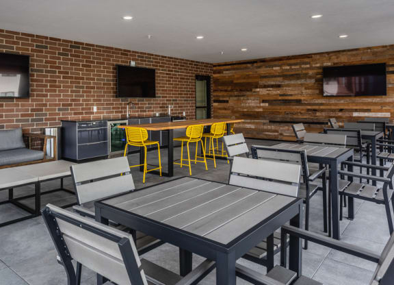 Sky lounge with outdoor furniture, tables and chairs, and three TV's.