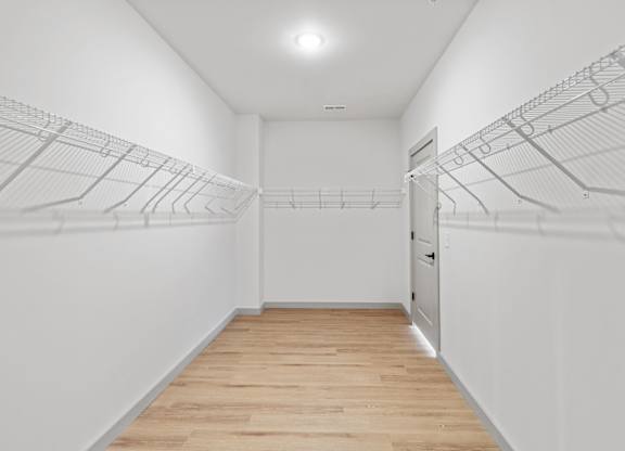 A well-lit long hallway closet with a plain white wall extends to a closed door at the far end.