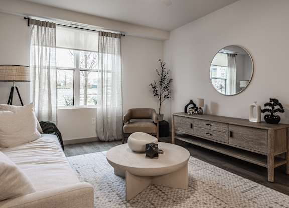 The living room offers a white sofa, a round accent table, and a closed wooden storage cabinet.