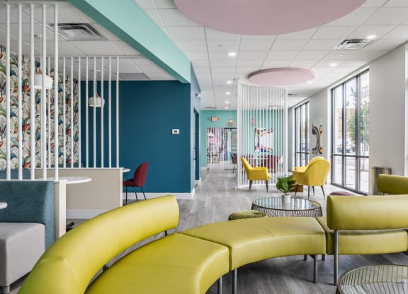 A green couch on hardwood-style floorings, next to tables and chairs in a co-working lounge.