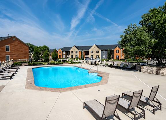 A swimming pool surrounded by lounge chairs and buildings in the background.