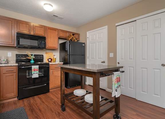 A kitchen with a black fridge and oven, wooden cabinets, and a wooden island with a towel hanging on it.