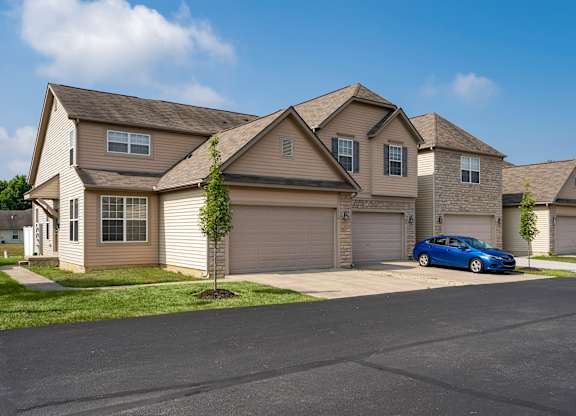 A blue car is parked in front of a house with a tree.