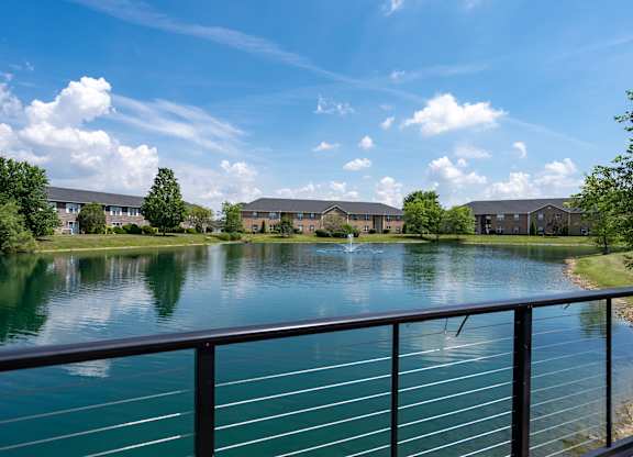 A serene lake surrounded by buildings and trees under a clear blue sky.