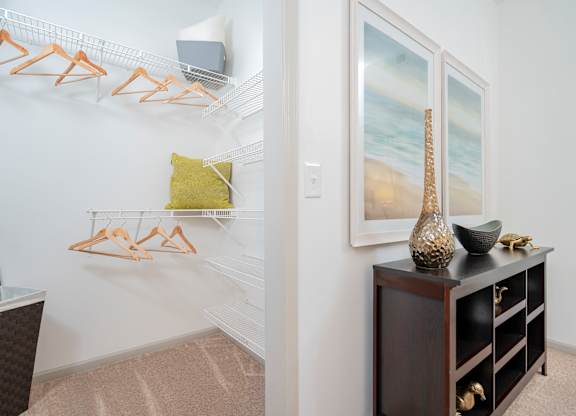 A room with a white wall and a wooden shelf with a vase on it.