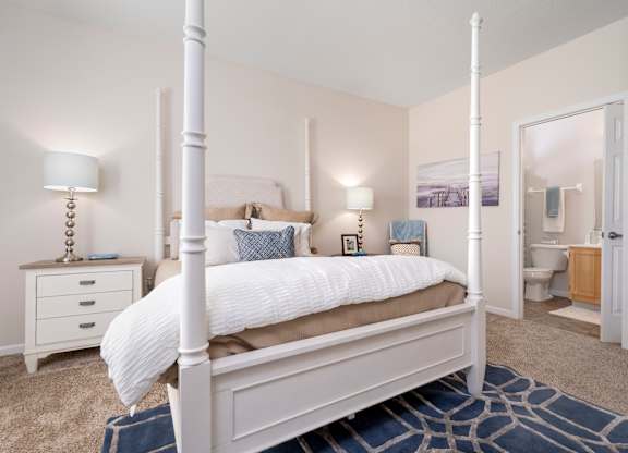 A white four poster bed with a white bedspread and pillow.