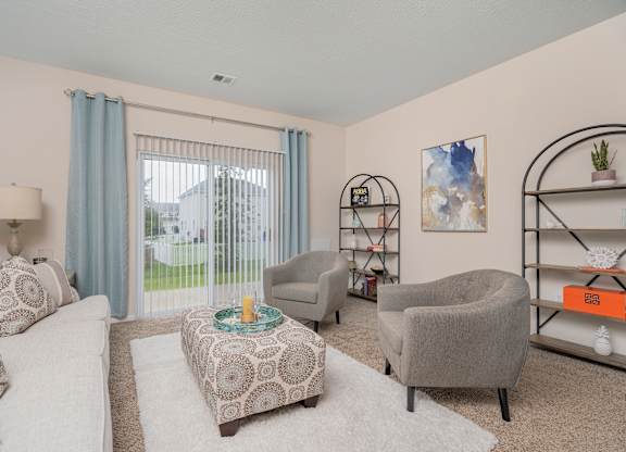 A living room with a white couch, grey armchair, and a patterned ottoman.