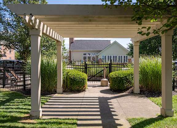 A white pergola with four pillars and a black gate in the foreground.