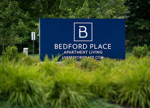 A blue sign for Bedford Place Apartment Living in front of some greenery.