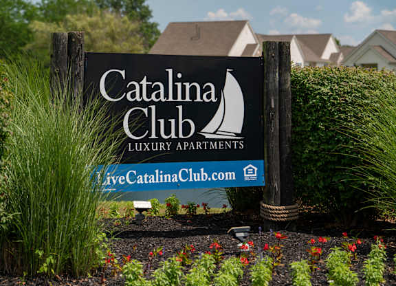 A sign for the Catalina Club Luxury Apartments is displayed in front of some greenery.