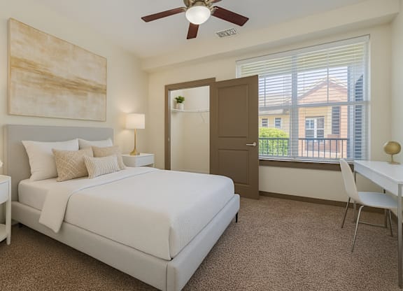 A bedroom with a large bed, a ceiling fan, and a painting on the wall.
