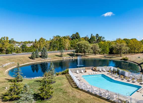 A large outdoor swimming pool surrounded by a fence and a smaller pond.