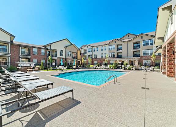 A resort-style swimming pool with a sundeck, lounge chairs, and well-kept landscaping.
