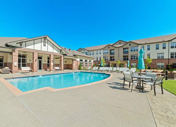 The resort-style swimming pool and sundeck at Austin Park Apartments feature shaded tables and comfortable lounge chairs.