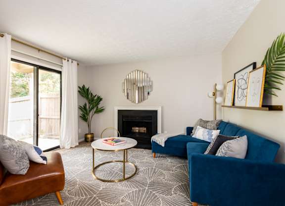 A living room featuring a blue couch, a fireplace, stylish decor, and a sliding glass door.