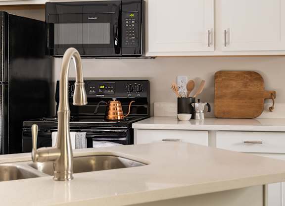 A kitchen equipped with black appliances, sleek white cabinets, and two barstools.