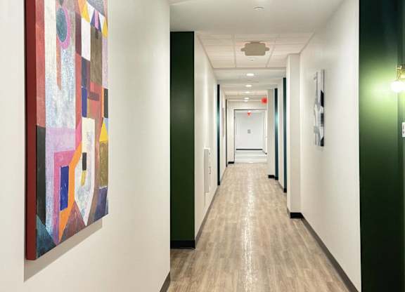 A hallway with a vibrant, colorful painting on the wall, leading to a corridor with green and white accents.