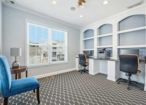 A room with a blue chair in front of a desk with a lamp on it.