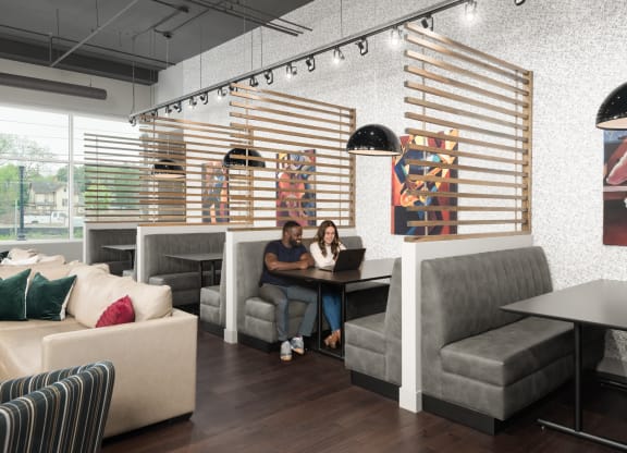 Co-working lounge with booth tables next to a beige couch, and light fixtures,