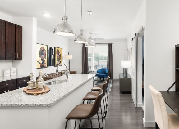 A kitchen with a spacious island with three barstools, next to a living room at Madamore Apartments.