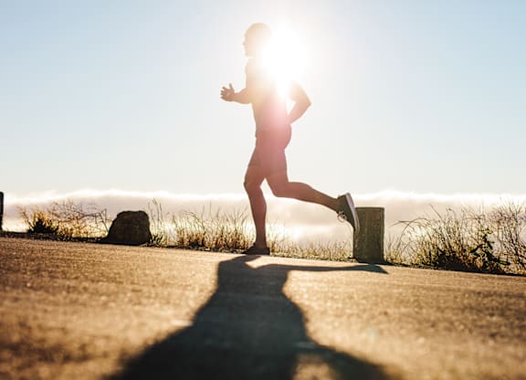 A person is running on a road with their shadow visible on the ground.