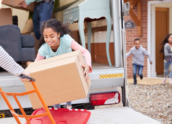 A woman is helping a girl to load a box into a moving truck.