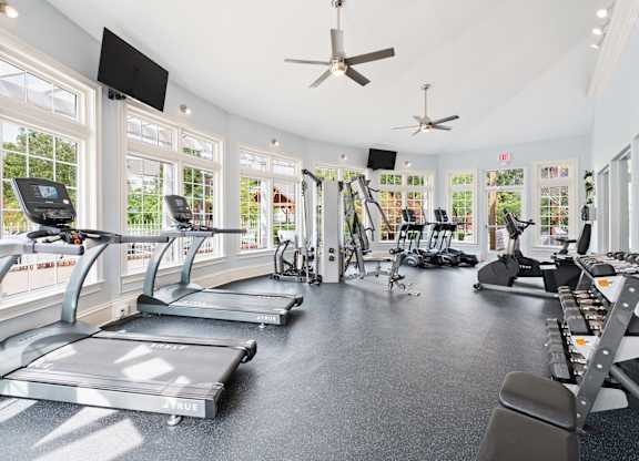 A fitness center equipped with cardio machines and weights surrounded by windows at Reserve at Hamburg.