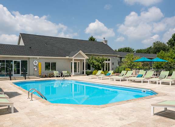 Swimming pool at The Coleman in Canal Winchester, OH, with chaise lounge chairs, sun umbrellas, and a modern gray building in the background