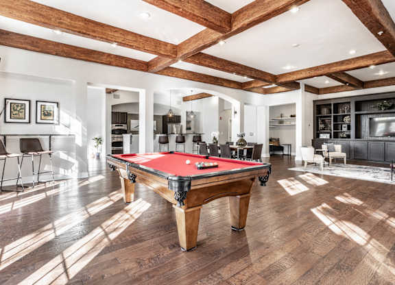 A pool table is in the middle of a room with wooden floors and a high ceiling.