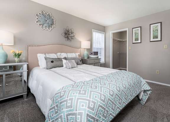 A furnished bedroom with a closet, carpeted flooring, a window, and decor.
