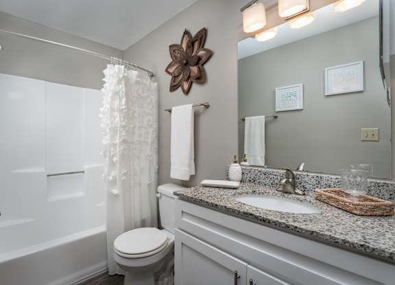 A bathroom at The Oaks with a vanity and a mirror, a white tub, and stylish decor.