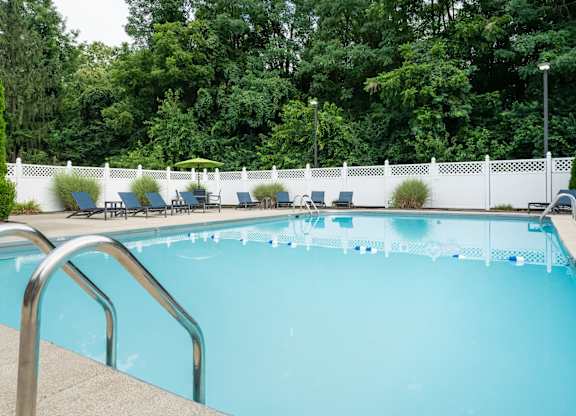 A swimming pool in Reynoldsburg, OH surrounded by blue chairs, a white fence, and large trees.